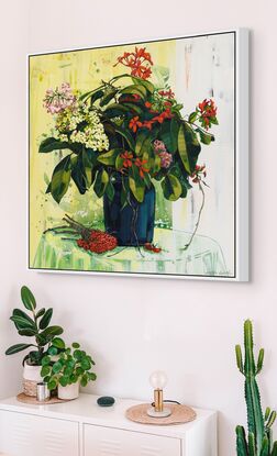 A framed limited edition canvas print in a white wood floating frame of an original still life painting of flowers in yellows, greens , reds and oranges in a glass vase