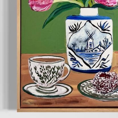 . The vase itself features a picturesque landscape of a Dutch windmill by a lakeside. Accompanying the scene is a cup of English milk tea and a delicious Lamington cake on a ceramic plate. The artwork conveys a sense of warmth and comfort, blending both Dutch and English elements seamlessly. 