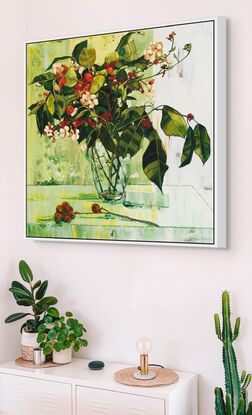 A framed limited edition canvas print in a white wood floating frame of an original still life painting of flowers in yellows, greens , reds and oranges in a glass vase