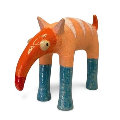 The Peachy Snoutosaurus is a charming ceramic creature with a rotund, striped body in soft orange hues, balanced on four sturdy blue legs. Its most striking feature is an elongated, trunk-like snout that curves dramatically upward, ending in a vibrant red tip. The eyes give this whimsical sculpture a watchful and endearing presence, enhancing its playful and curious character.