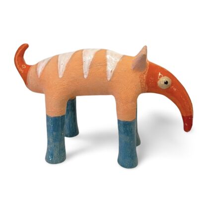 The Peachy Snoutosaurus is a charming ceramic creature with a rotund, striped body in soft orange hues, balanced on four sturdy blue legs. Its most striking feature is an elongated, trunk-like snout that curves dramatically upward, ending in a vibrant red tip. The eyes give this whimsical sculpture a watchful and endearing presence, enhancing its playful and curious character.