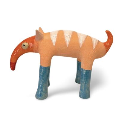 The Peachy Snoutosaurus is a charming ceramic creature with a rotund, striped body in soft orange hues, balanced on four sturdy blue legs. Its most striking feature is an elongated, trunk-like snout that curves dramatically upward, ending in a vibrant red tip. The eyes give this whimsical sculpture a watchful and endearing presence, enhancing its playful and curious character.