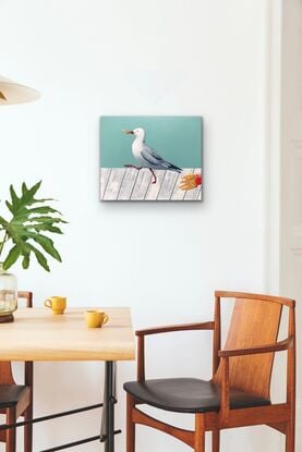 A seagull with chips in its beak marching away from a paper cup of fries laying on a whiter wooden table.