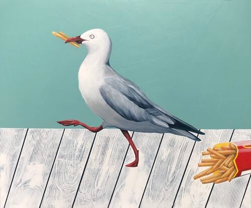 A seagull with chips in its beak marching away from a paper cup of fries laying on a whiter wooden table.