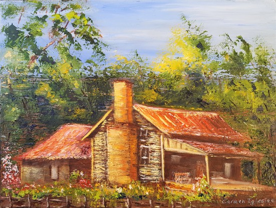 An old house, with red tin roof and yellow walls, in the middle of the bush. A chimney on the side of the house. A veranda at the front. Trees and wild flowers around it. 