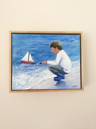 Young boy sailing his new boat for the first time. Main colours are blue and white with a touch of mauve and pink in the sand where his blue boots are reflected.