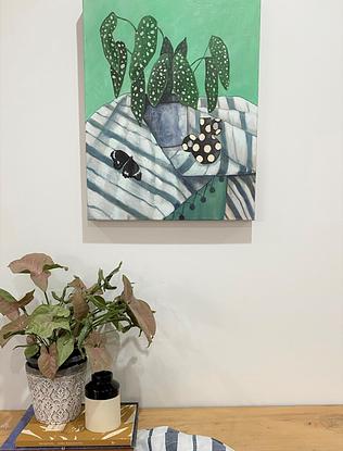 Spotty house plant in a denim blue coloured pot, sitting on top of a blue and white stripey tablecloth.  There is a black and white spotty pot off to one side, and a black and white moth in the foreground.  