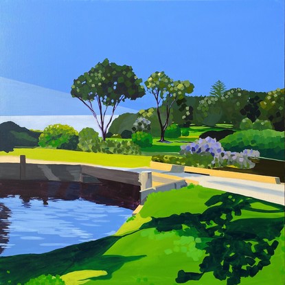 Shadows on grass beside blue lake with bridge and trees in background with blue sky