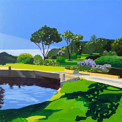 Shadows on grass beside blue lake with bridge and trees in background with blue sky